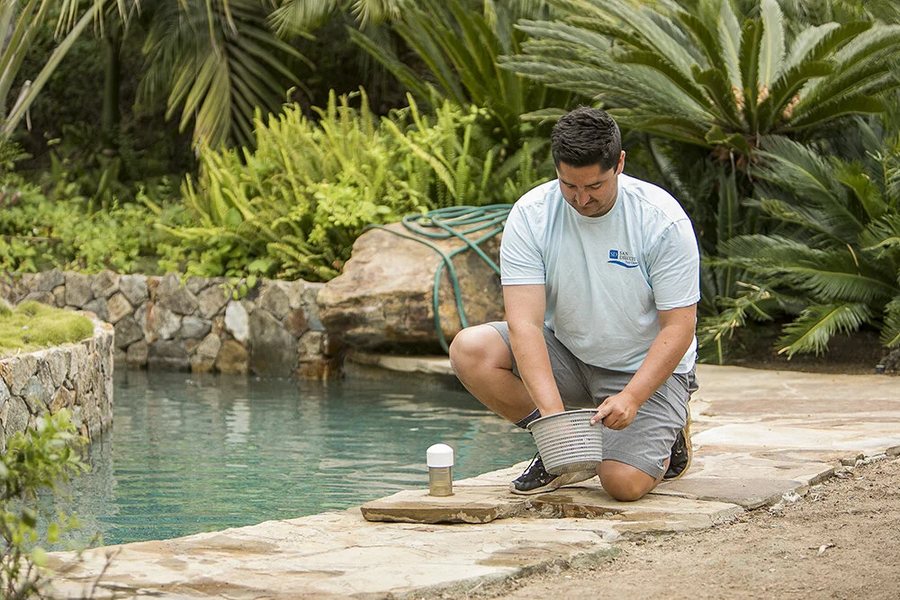 Technician skimming a rock-lined pool on weekly service in San Diego County